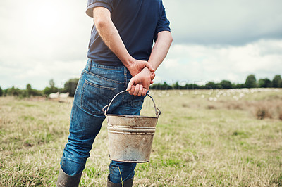 Buy stock photo Rearview shot of a unrecognizable farmer standing with his hands behind his back holding a bucket outside during the day
