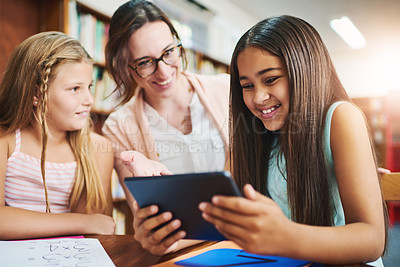 Buy stock photo Shot of two cheerful young school girls working together in a classroom with a digital tablet while being assisted by their teacher at school