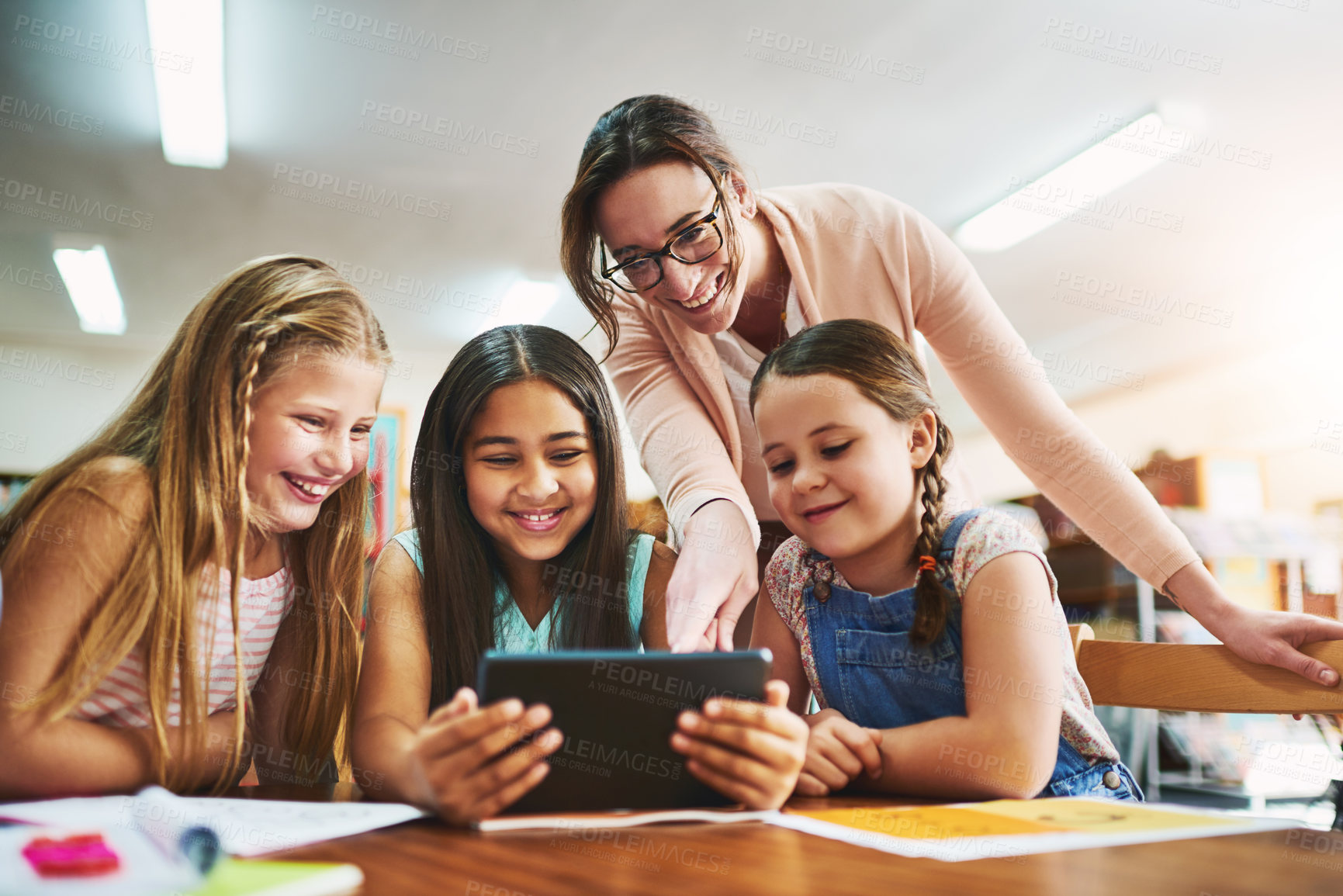 Buy stock photo Shot of a group of cheerful young school girls working together in a classroom with a digital tablet while being assisted by their teacher at school