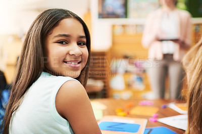 Buy stock photo Portrait of a cheerful young schoolgirl turning and looking back while being seated inside of a classroom during the day