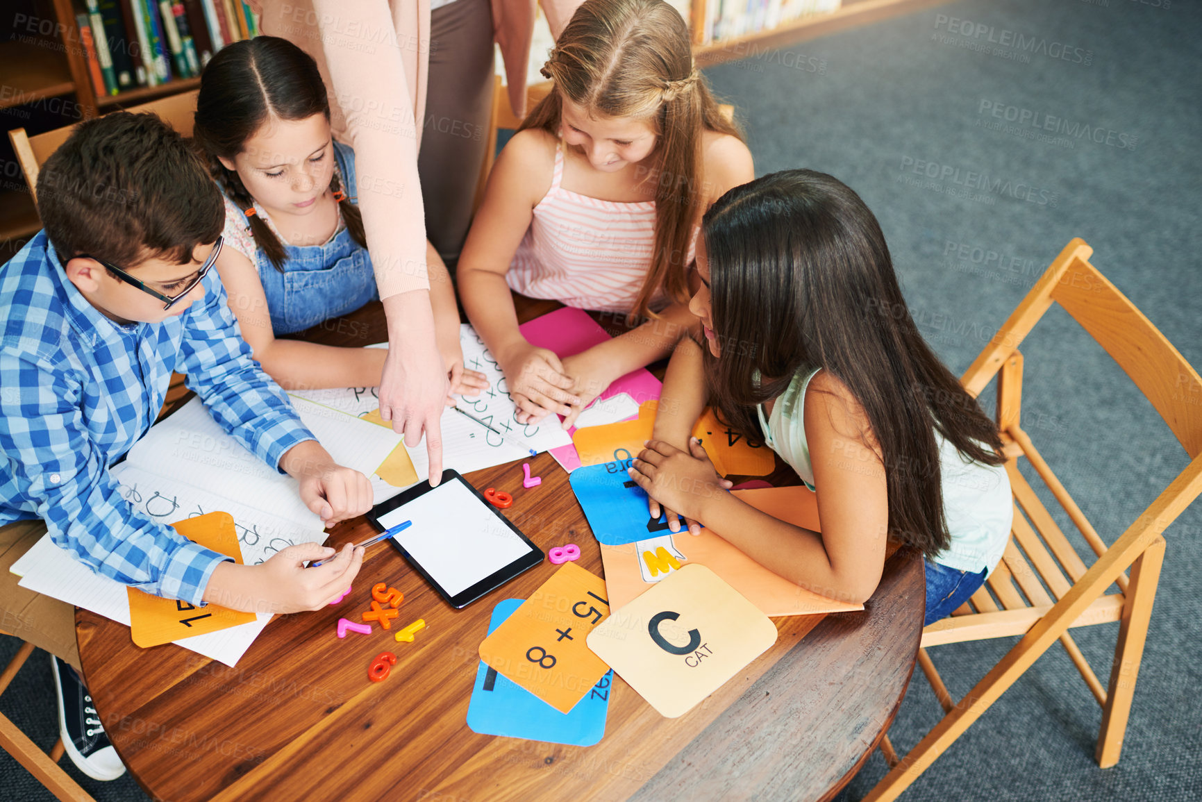 Buy stock photo Shot of a group of cheerful young school girls working together in a classroom with a digital tablet while being assisted by their teacher at school