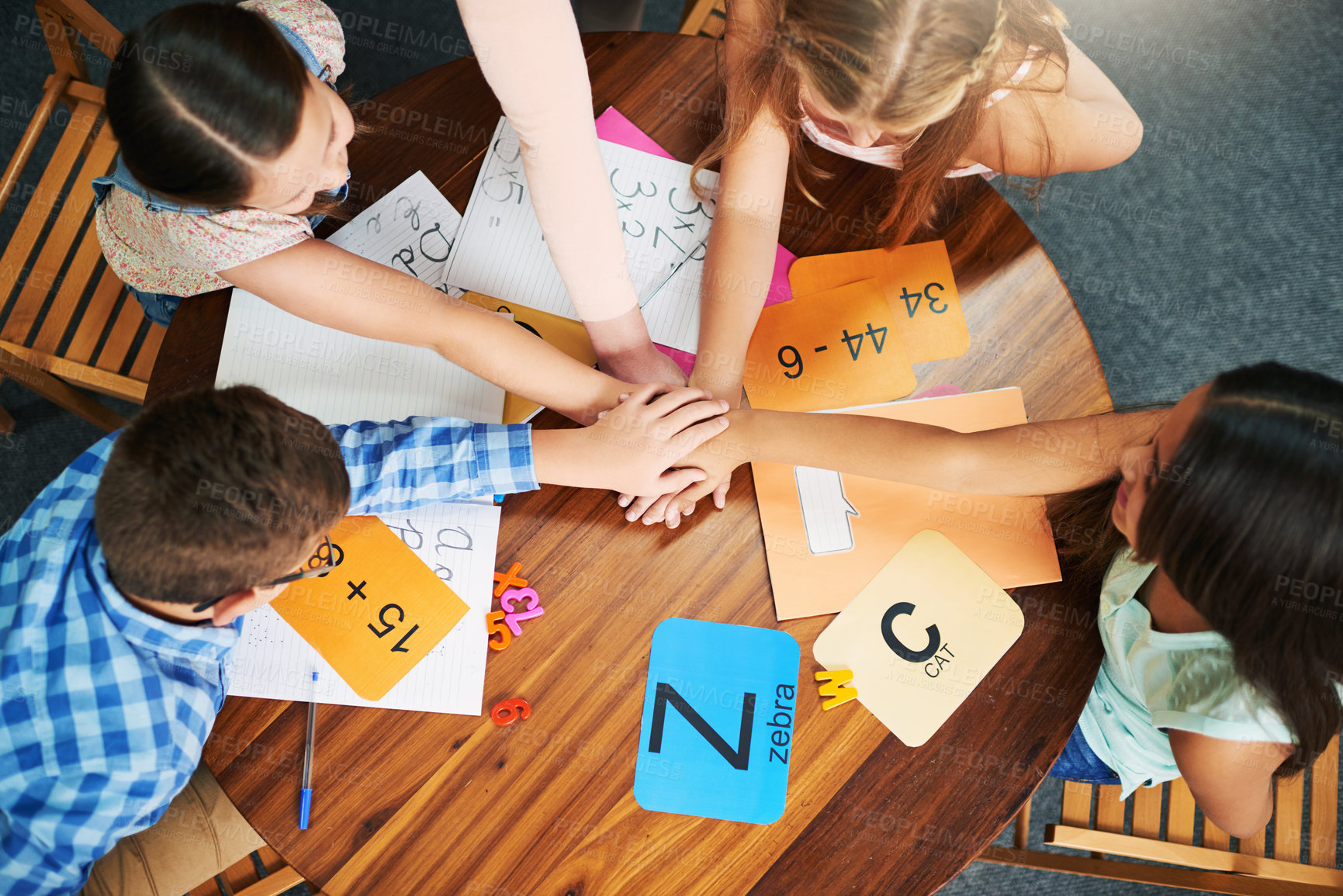 Buy stock photo High angle shot of a group of cheerful school children forming a huddle with their hands inside of the classroom during the day