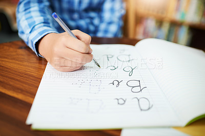 Buy stock photo Closeup of an unrecognizable young boy working and writing inside of a book at school during the day