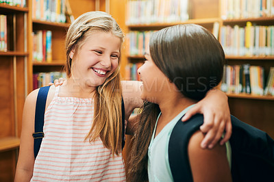 Buy stock photo Shot of two cheerful young school girls standing arms around inside of a library at school during the day