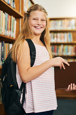 Buy stock photo Portrait of a cheerful young girl reading a school book while standing inside of a library during the day