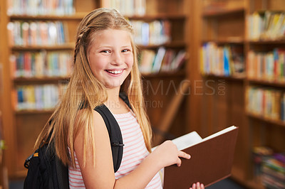 Buy stock photo Portrait of a cheerful young girl reading a school book while standing inside of a library during the day