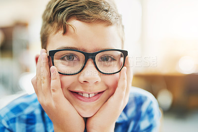 Buy stock photo Portrait of a cheerful young boy  resting his face in his hands while being seated inside of a classroom during the day