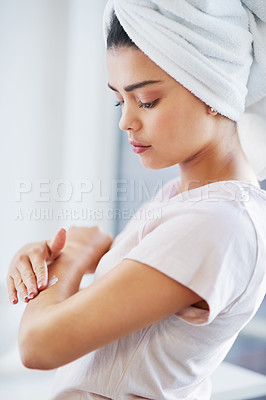 Buy stock photo Shot of a beautiful young woman applying moisturizer to her skin in the bathroom at home