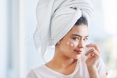 Buy stock photo Portrait of a beautiful young woman applying moisturizer to her skin in the bathroom at home