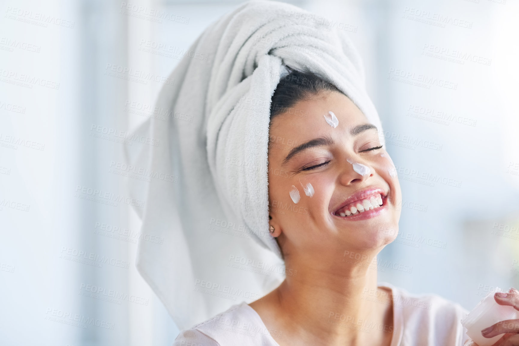 Buy stock photo Shot of a beautiful young woman applying moisturizer to her skin in the bathroom at home