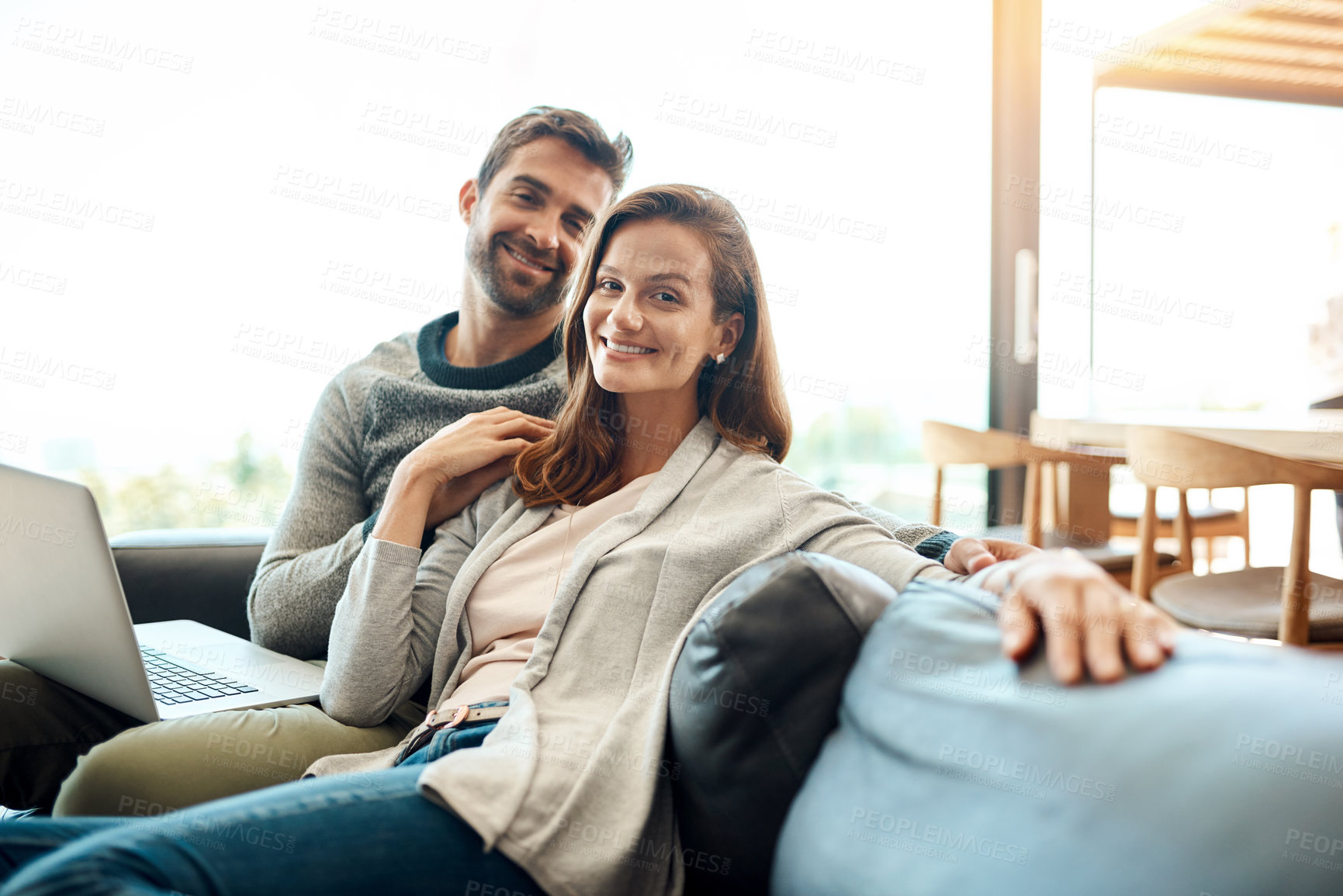 Buy stock photo Portrait of an affectionate young couple using a laptop while relaxing on their sofa at home