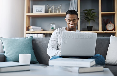 Buy stock photo Shot of a handsome young man using his laptop while sitting on a sofa at home