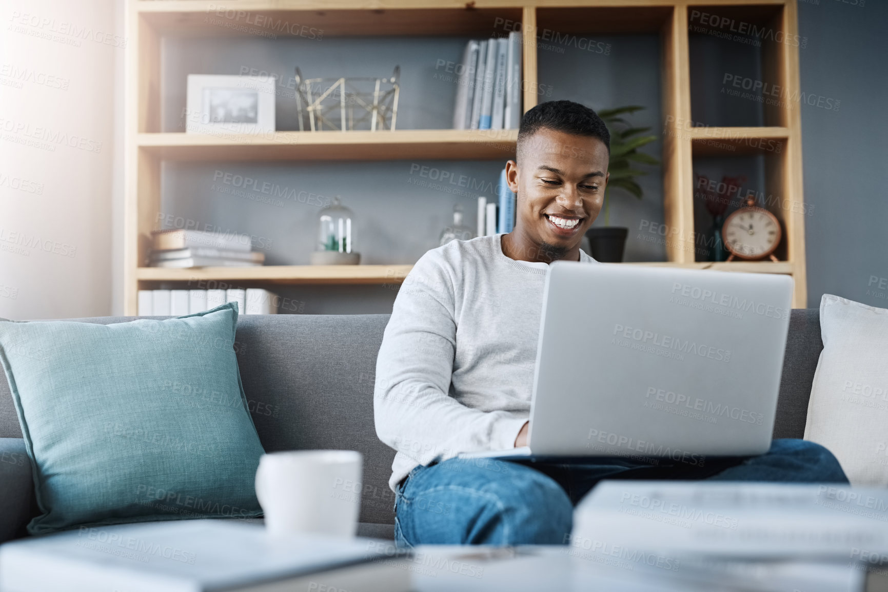 Buy stock photo Shot of a handsome young man  using his laptop while sitting on a sofa at home