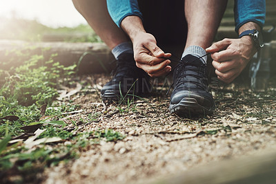 Buy stock photo Close up shot of an unrecognizable man tying up his shoe laces on a hiking trail