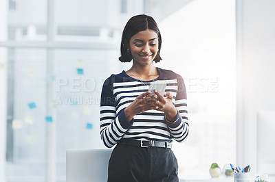 Buy stock photo Shot of a young businesswoman standing and using her cellphone at the office