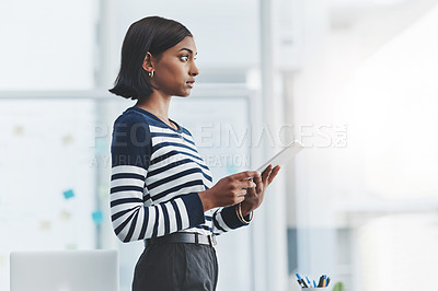 Buy stock photo Shot of a young businesswoman holding a digital tablet and looking out the window in her office