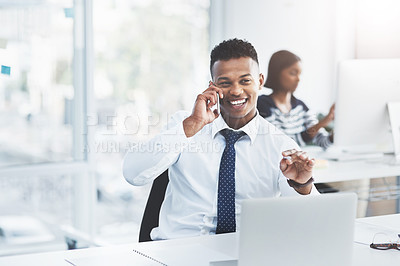 Buy stock photo Shot of a young businessman making a phone call at his office desk with a colleague working in the background