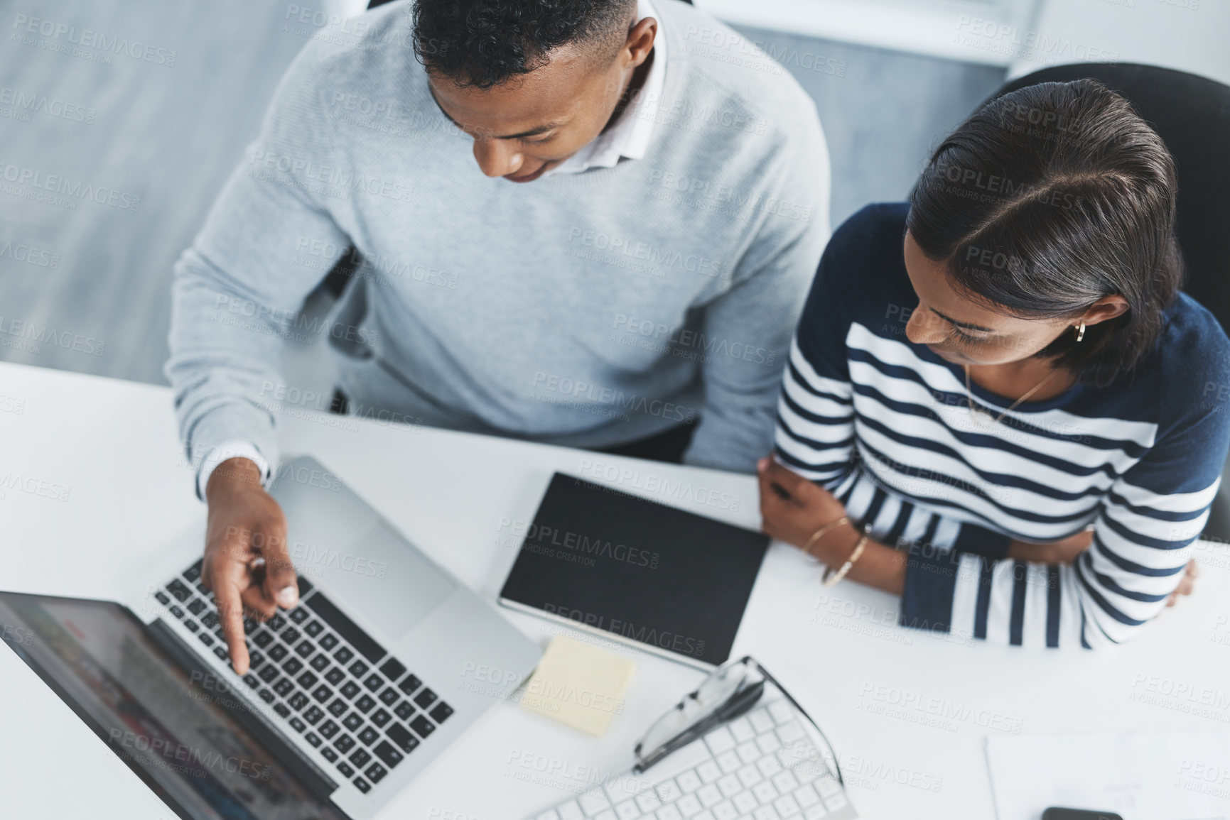 Buy stock photo High angle shot of two young businesspeople going through figures on a laptop at their office desk