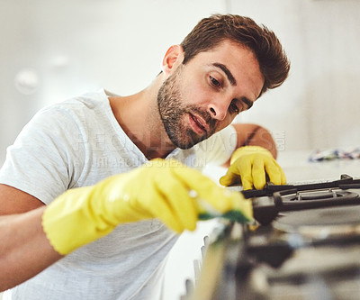 Buy stock photo Cropped shot of a handsome young man carefully cleaning the stove in his kitchen