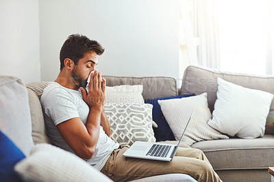 Buy stock photo Cropped shot of a handsome young man sneezing into a tissue while trying to work on his laptop at home