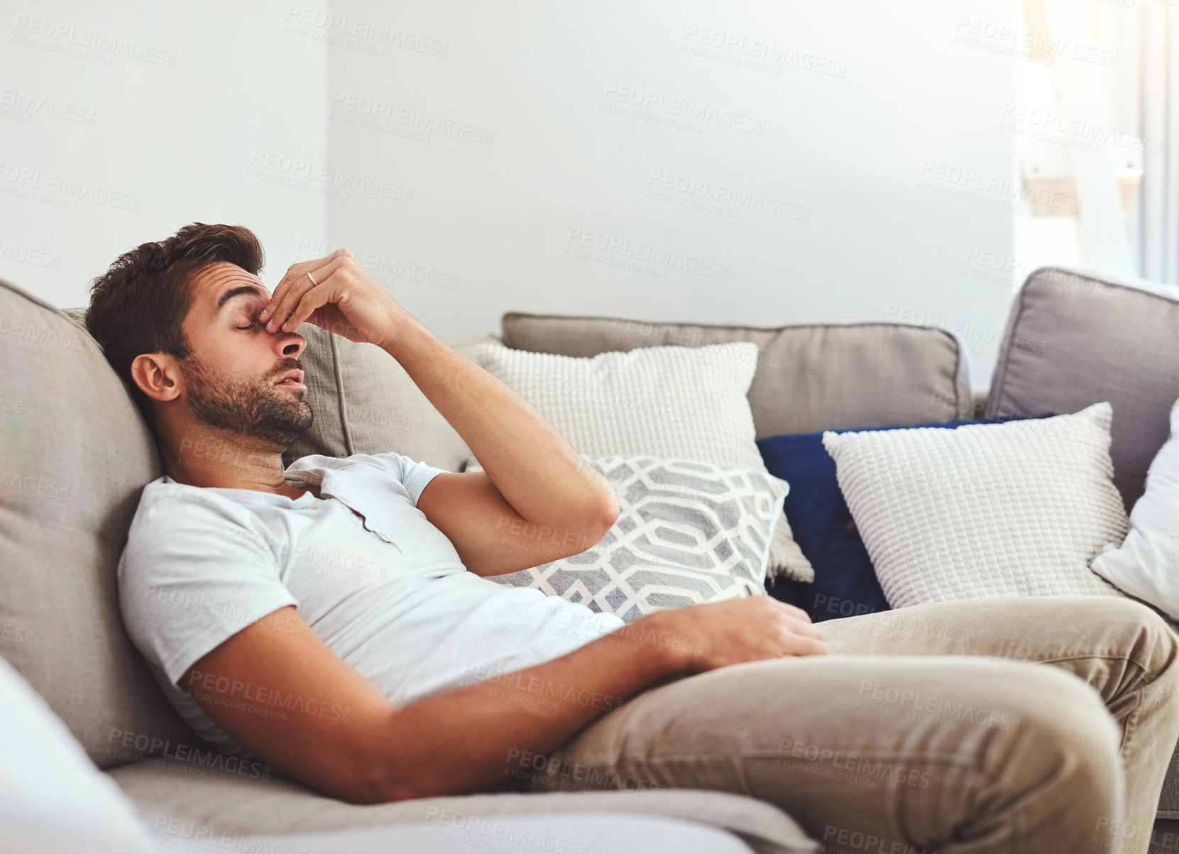 Buy stock photo Cropped shot of a handsome young man holding his nose while lying on a couch at home during the day