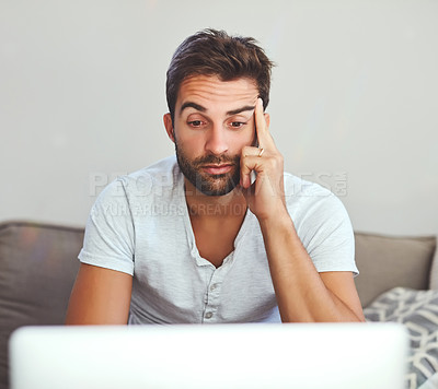 Buy stock photo Cropped shot of a handsome young man looking bored while working on his laptop at home