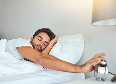 Buy stock photo Cropped shot of a tired young man sleeping in his bed while turning off the alarm clock