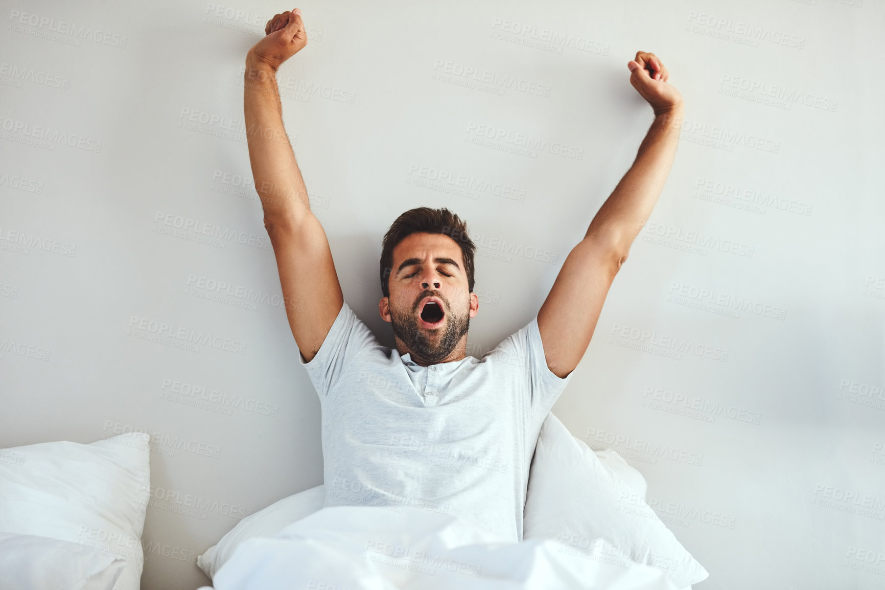 Buy stock photo Cropped shot of a tired young man stretching and yawning after waking up from a good night's sleep