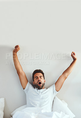 Buy stock photo Cropped shot of a tired young man stretching and yawning after waking up from a good night's sleep