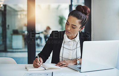 Buy stock photo Shot of a young businesswoman making notes at her desk in a modern office