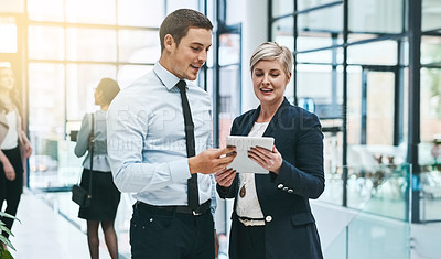 Buy stock photo Cropped shot of two young businesspeople working on a digital tablet in a busy office