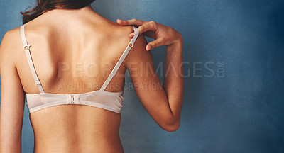 Buy stock photo Cropped studio shot of a young woman removing her bra against a blue background