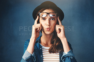Buy stock photo Studio shot of an attractive young woman lifting her glasses and pouting against a blue background