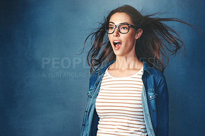Buy stock photo Studio shot of a young woman with air being blown in her face against a blue background