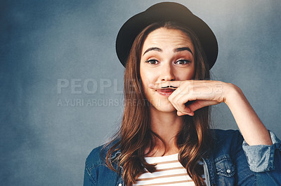 Buy stock photo Studio shot of an attractive young woman making a finger moustache against a blue background