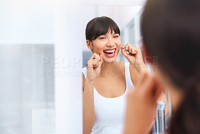 Buy stock photo Shot of a cheerful attractive young woman flossing her teeth while looking at her reflexion in a mirror at home