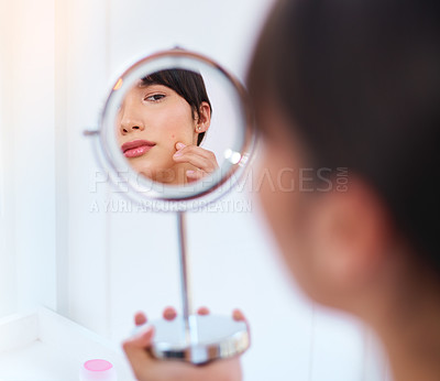 Buy stock photo Shot of a stressed out attractive young woman noticing a zit on her face while looking at her refection in a mirror at home during the day