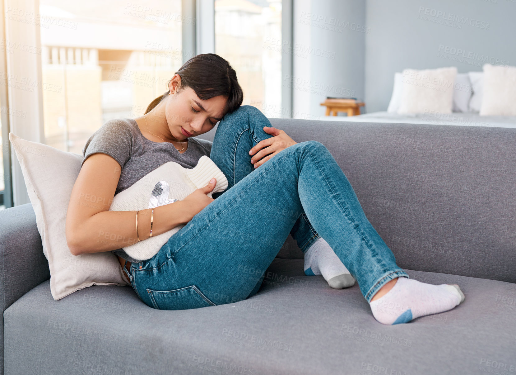 Buy stock photo Stomach pain, stress or girl on sofa with hot water bottle for pms gas, constipation or period crisis at home. Tummy, digestion or anxiety in living room with heating pad for endometriosis or pcos