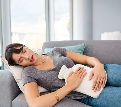 Buy stock photo Woman, sofa and pain with hot water bottle in home, abdominal cramps or menstrual issues. Endometriosis, cyst ovaries or uterus problems, resting in living room for comfort or menstruation relief 

