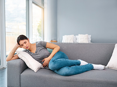 Buy stock photo Shot of a uncomfortable looking  young woman holding a water bottle tightly while trying to get rest on a sofa at home