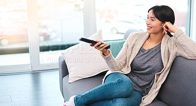Buy stock photo Shot of a cheerful young woman holding a remote to change channels while watching television at home