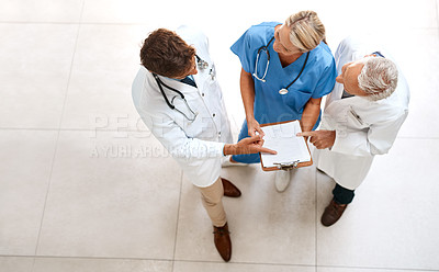 Buy stock photo High angle shot of a team of doctors brainstorming over a patient's file in the hospital foyer