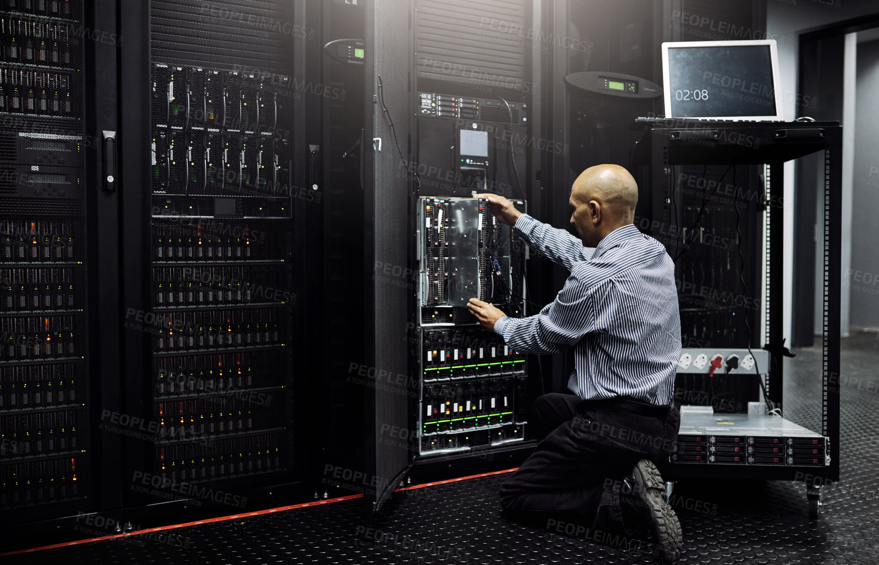 Buy stock photo Rearview shot of an IT technician repairing a computer in a data center