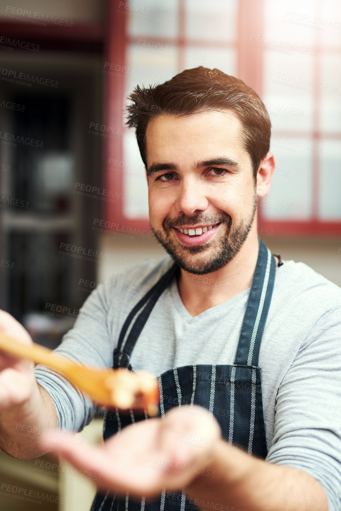 Buy stock photo Cropped portrait of a handsome young man offering you a taste while cooking in the kitchen