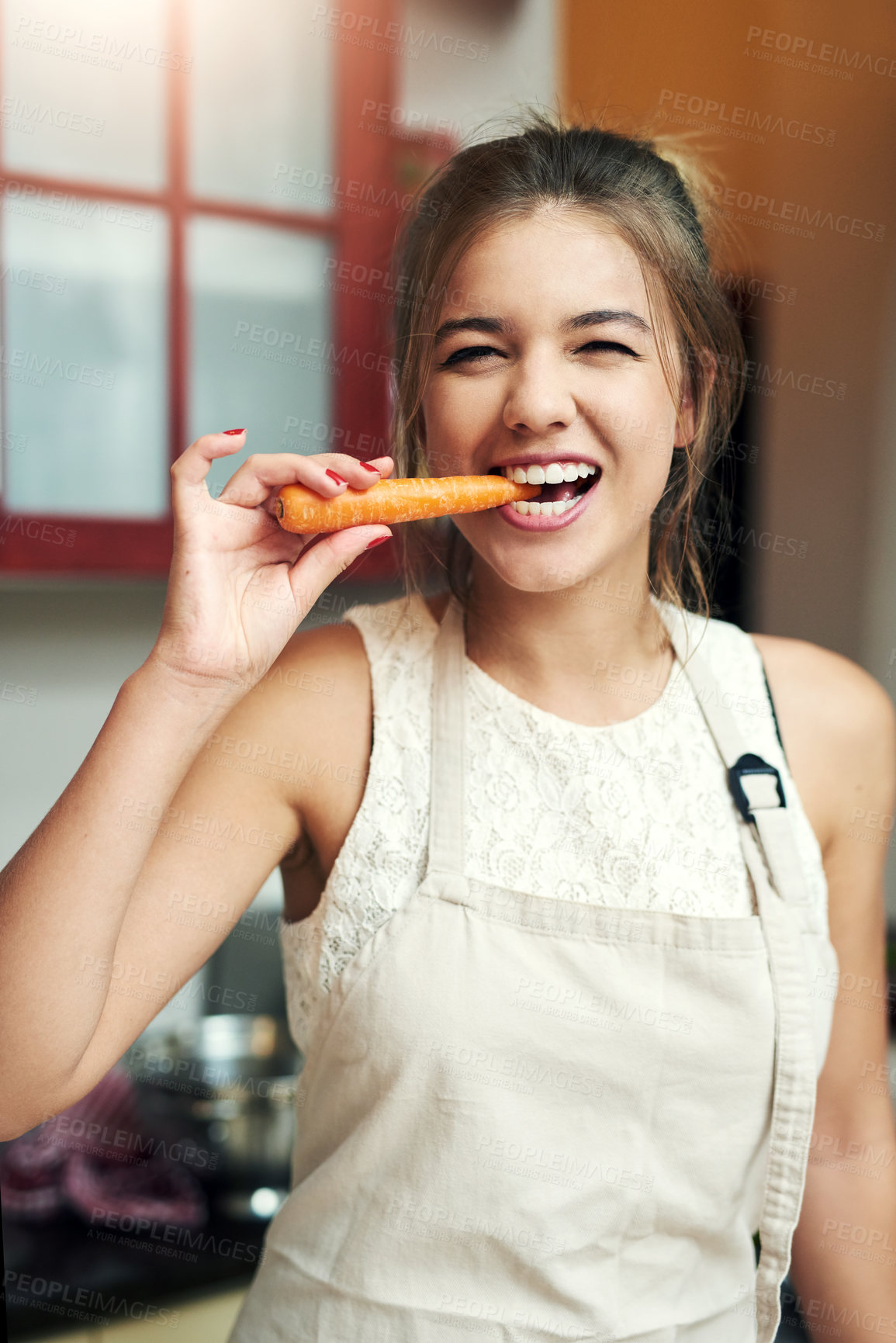 Buy stock photo Cropped portrait of an attractive young woman taking a bite of a carrot at home