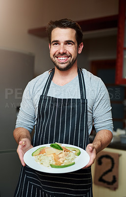 Buy stock photo Cropped portrait of a handsome young man serving food in the kitchen at home