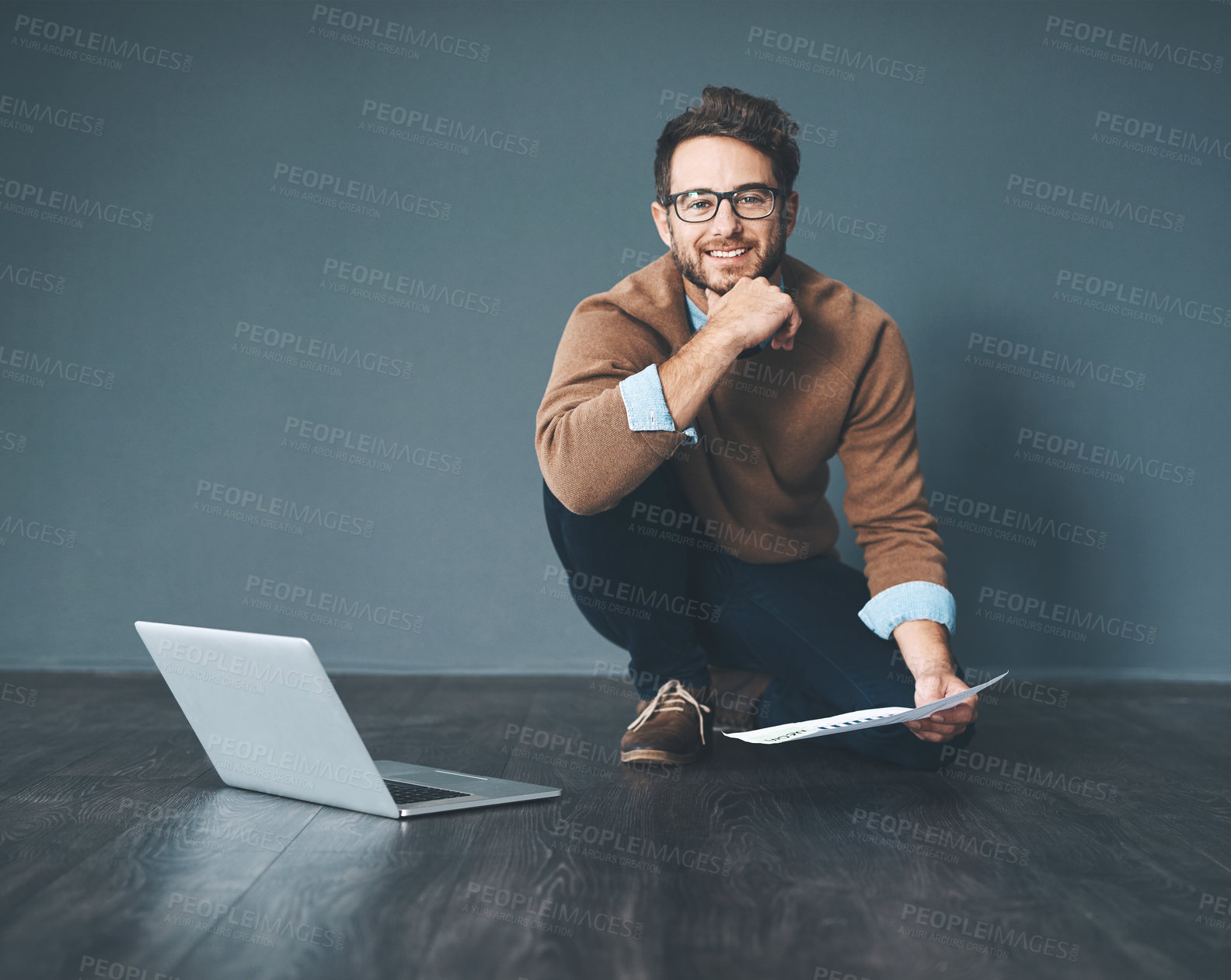 Buy stock photo Happy business man working on laptop, doing tax paperwork and going through finance document while sitting on floor in an office at work. Portrait of entrepreneur planning and completing a project