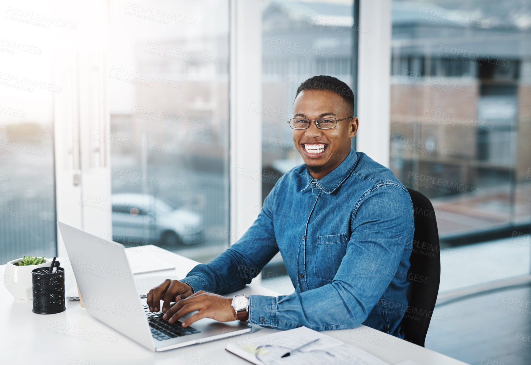 Buy stock photo Portrait, smile and black man in modern office with laptop, paperwork and happiness at desk. Businessman, technology and pride in workplace for internship, journalist and research for startup company