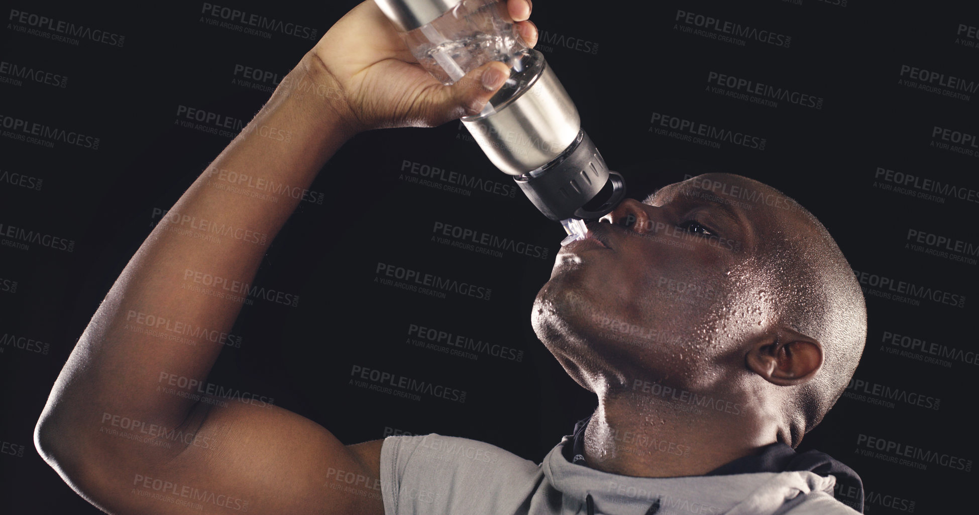 Buy stock photo Studio shot of a young sportsman drinking from a water bottle against a dark background