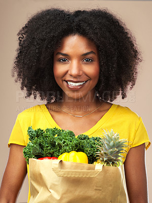Buy stock photo Studio shot of an attractive young woman holding a bag full of vegetables against a brown background